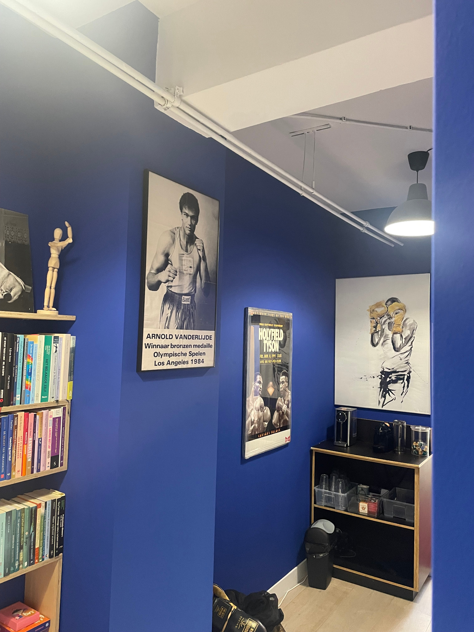 Blauwe muren met boksaffiches, boeken en een koffiehoek in de praktijk